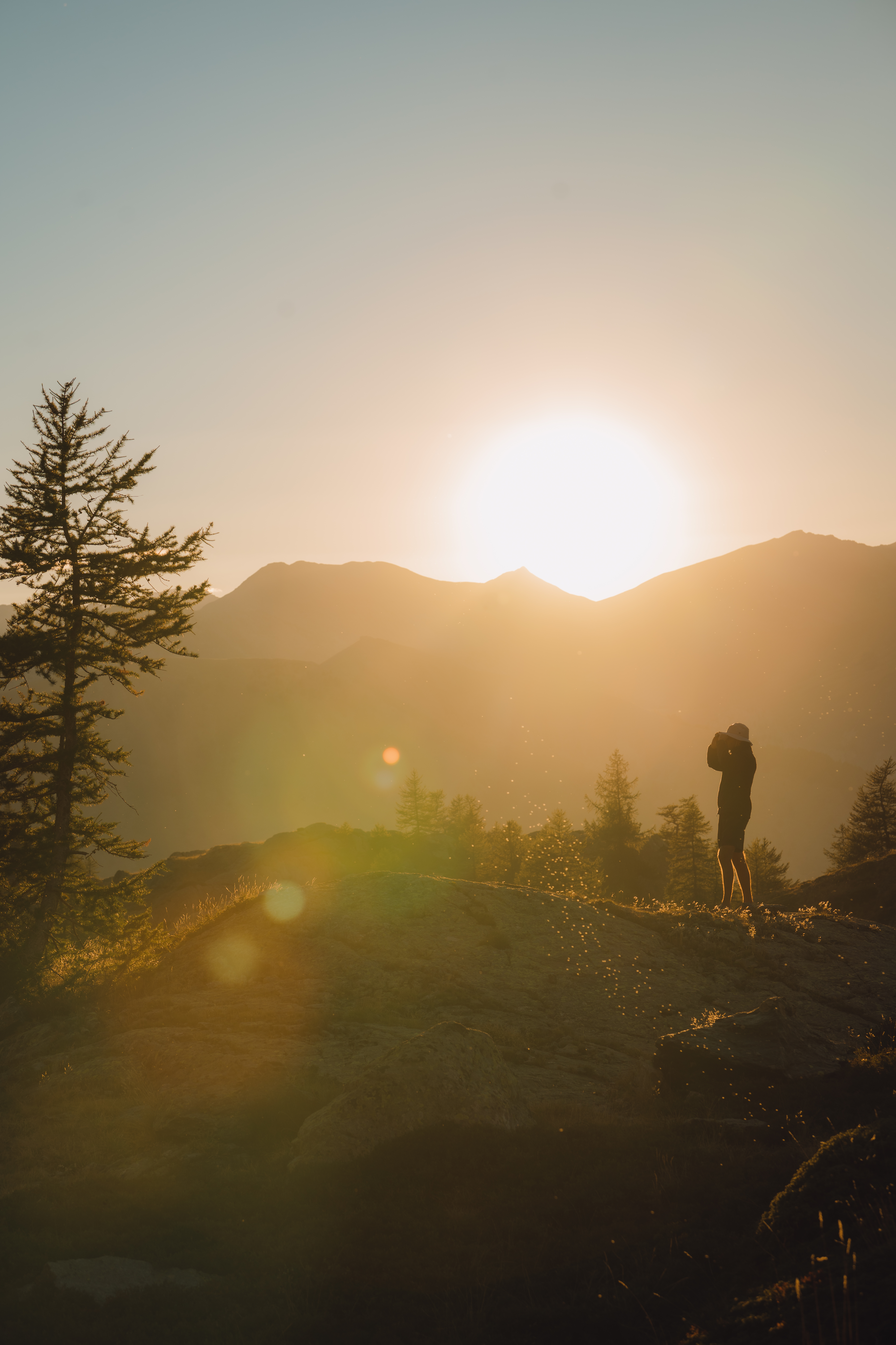 Un paysage de montagne au coucher du soleil avec une silhouette de personne prenant des photos.
