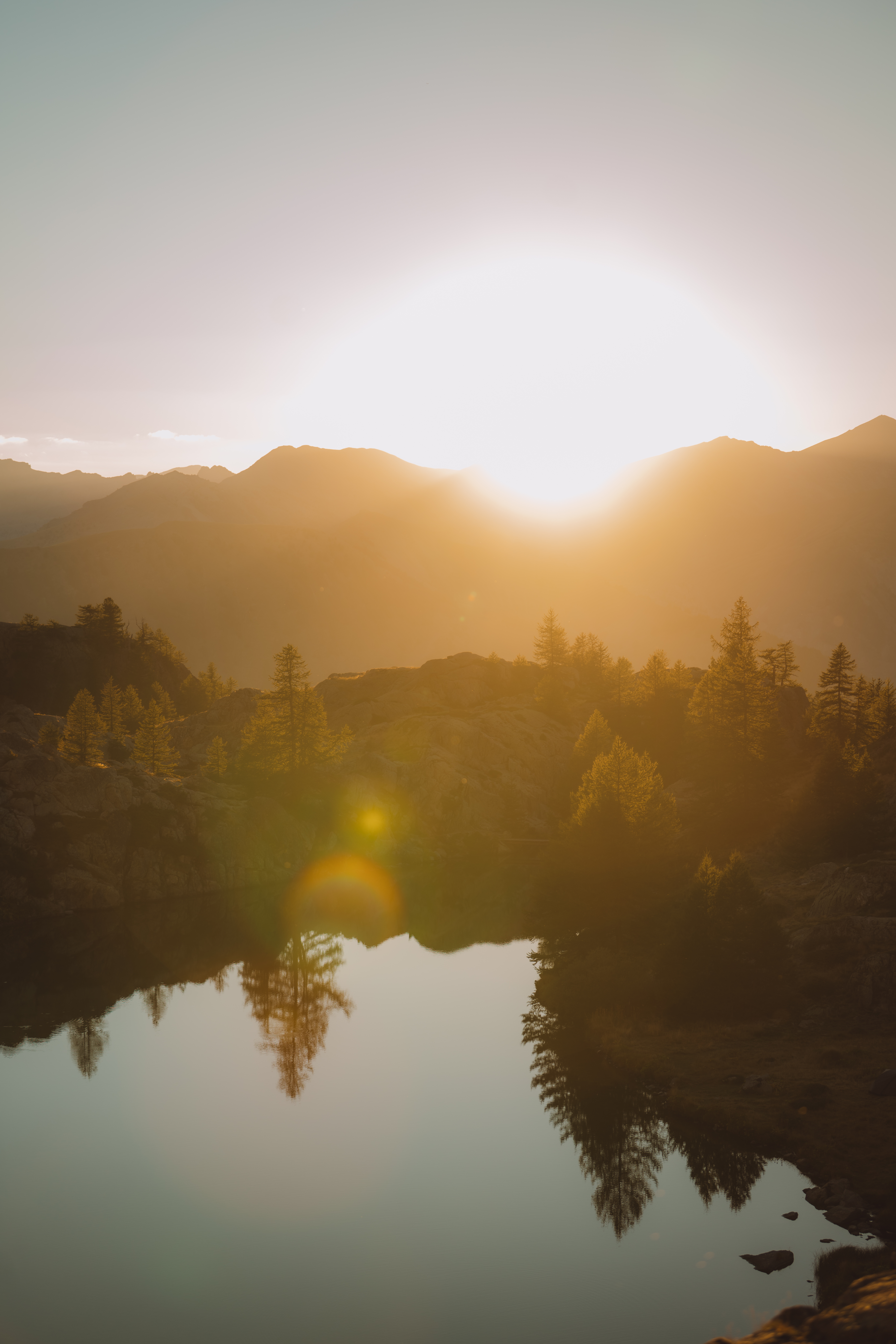 Lever de soleil sur des montagnes avec un lac réfléchissant en premier plan.