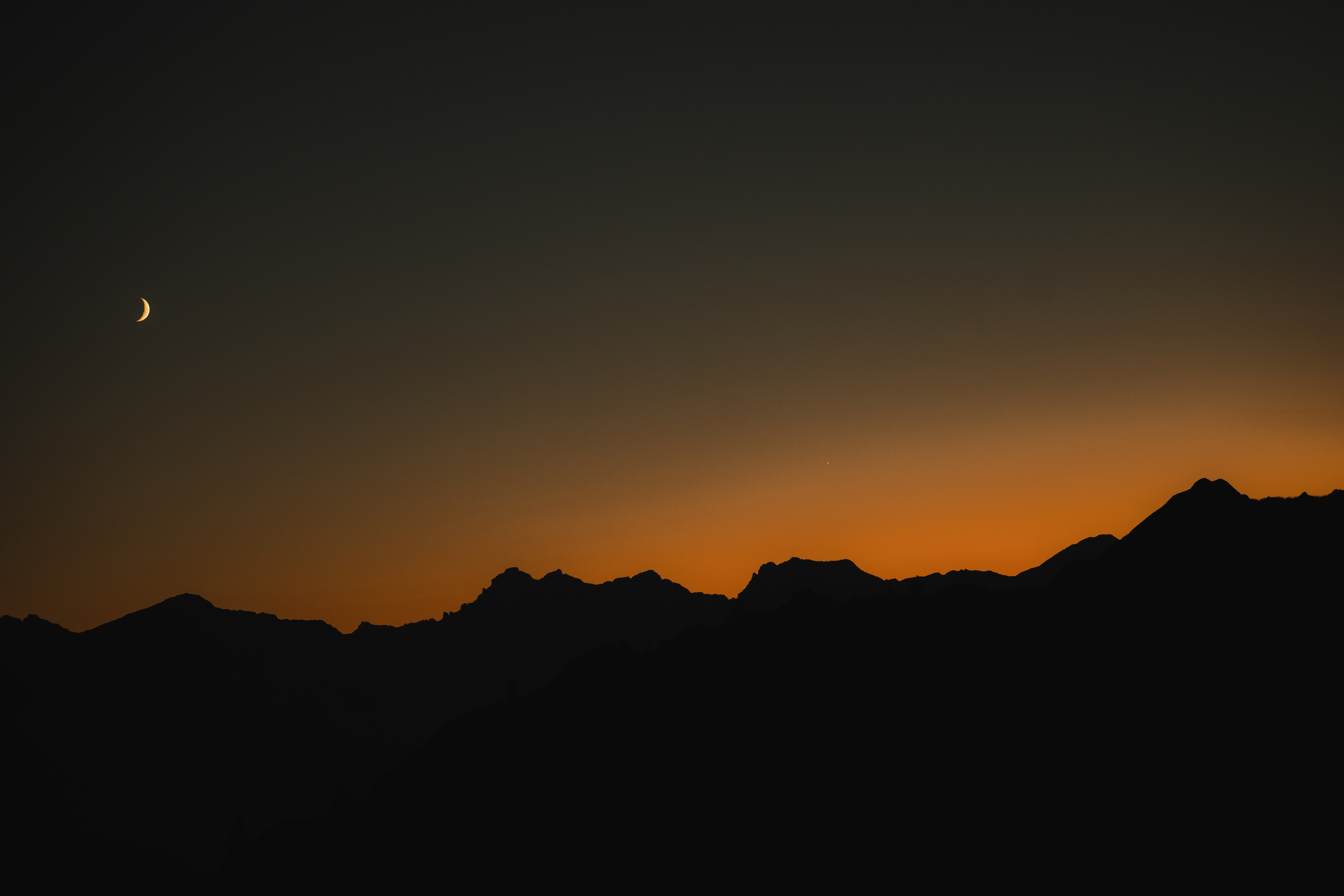 Coucher de soleil sur des montagnes avec une lune croissante dans le ciel.