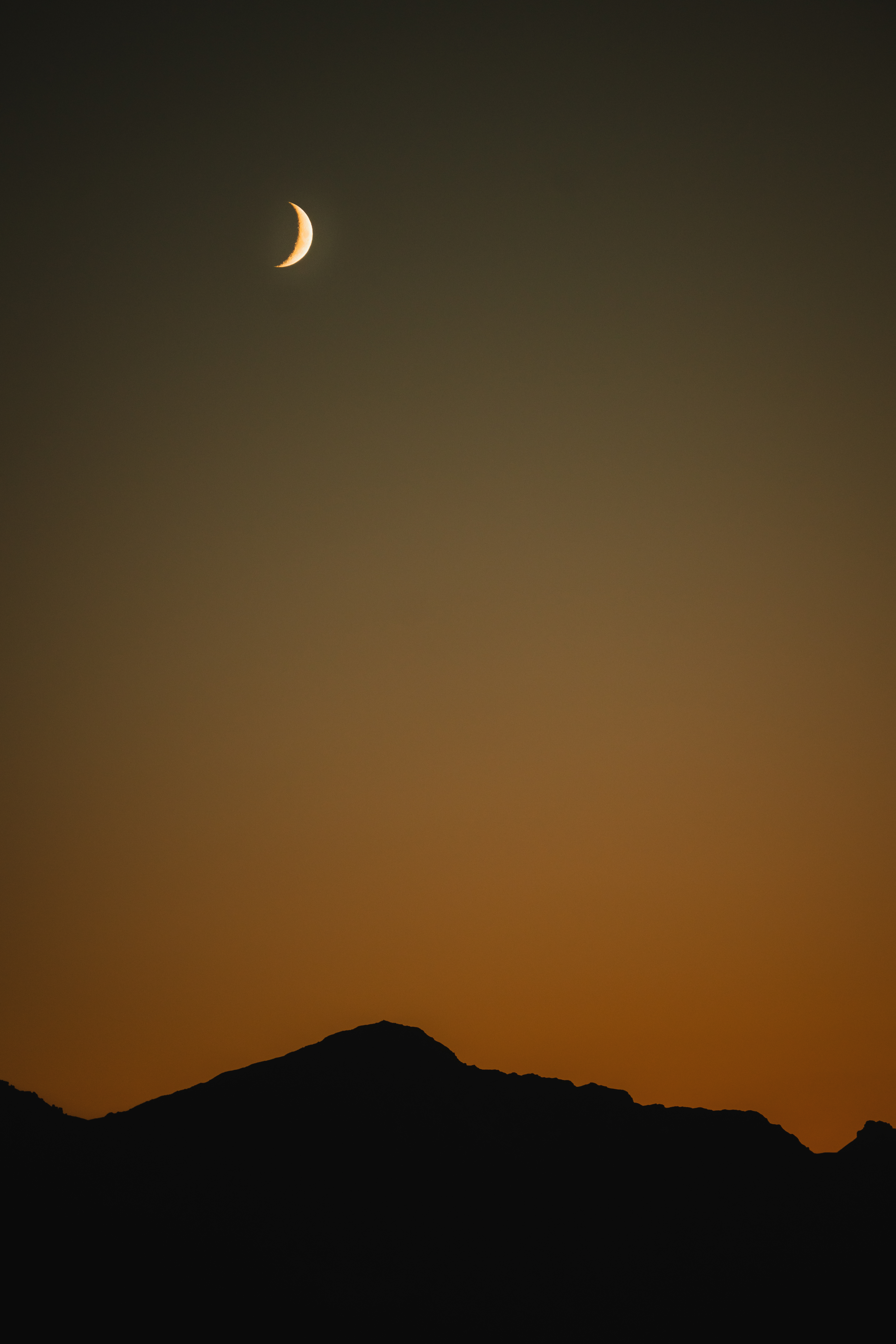 Ciel crépusculaire avec un croissant de lune au-dessus des montagnes silhouettées.