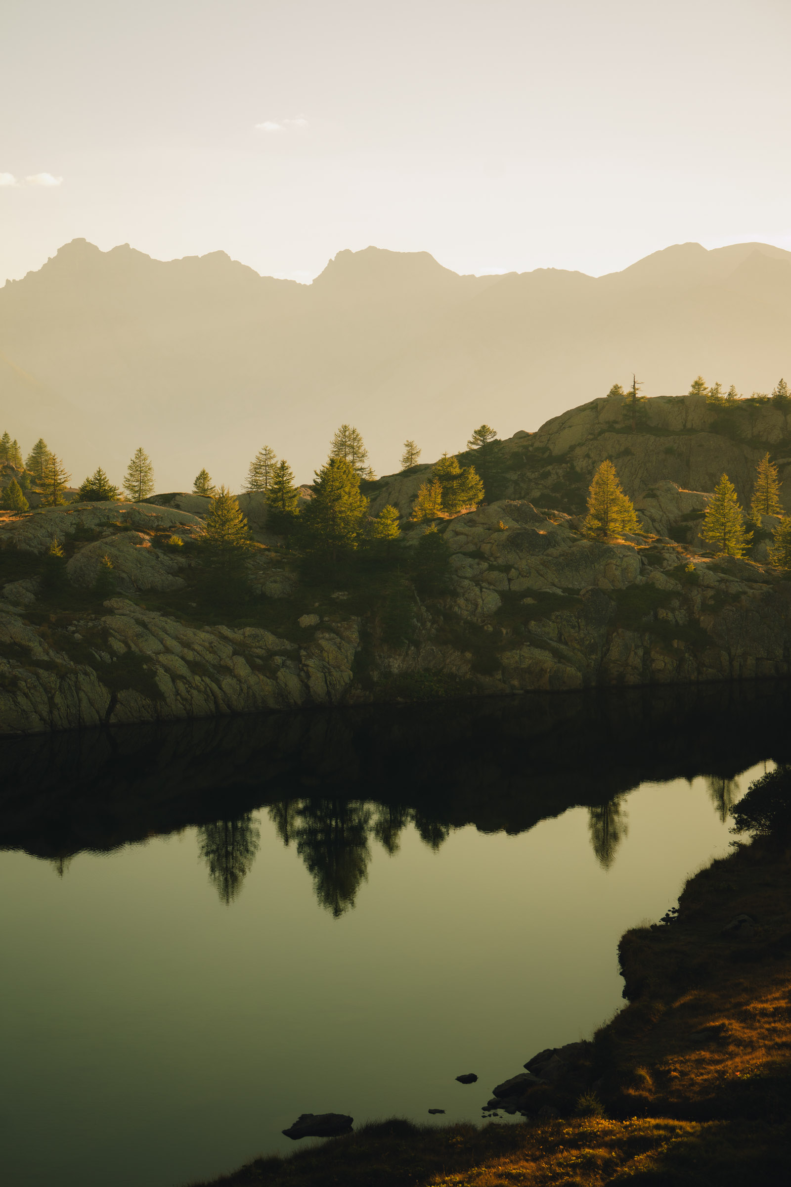 Reflet pittoresque des arbres sur un lac calme, entouré de montagnes au coucher du soleil.